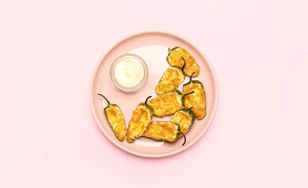 Plate with tasty jalapeno poppers and sauce on pink background