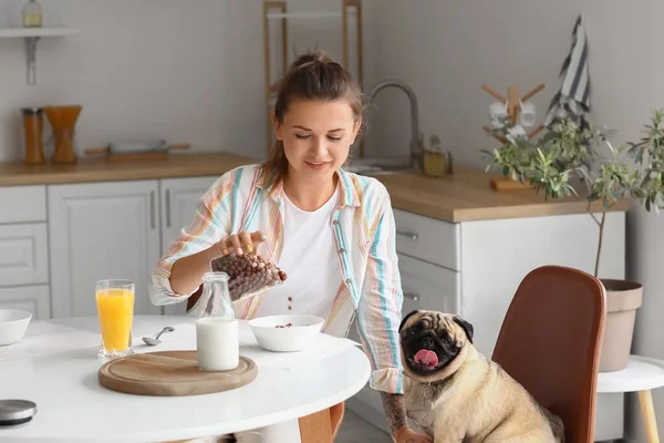 Young woman with cute pug dog having breakfast in kitchen