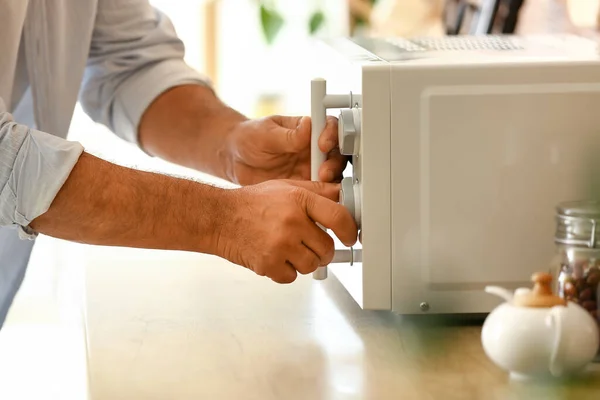 Mature man heating food in microwave oven, closeup