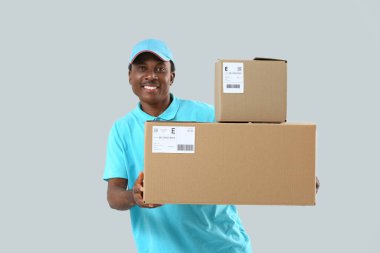 Gri arka planda paketleri olan Afro-Amerikalı teslimatçı.