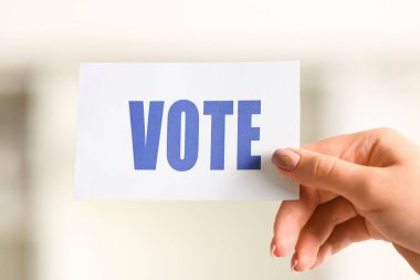 Oy kullanma merkezinde elinde VOTE yazılı kağıt tutan kadın, yakın plan