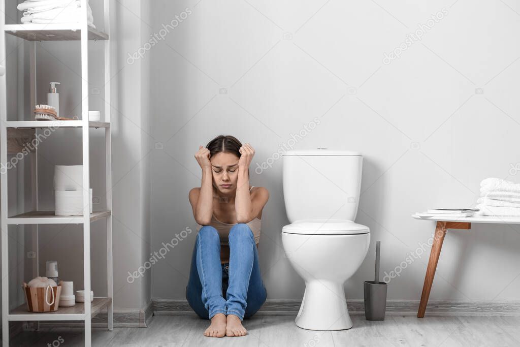 Young woman near toilet bowl in bathroom. Anorexia concept