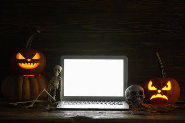 Cadılar Bayramı için oyulmuş balkabakları, koyu ahşap arka planda dizüstü bilgisayarla.