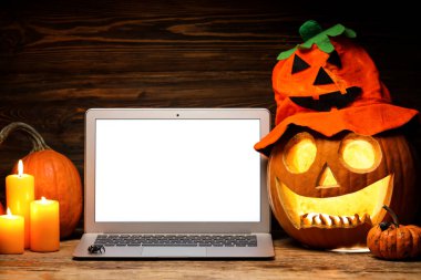 Cadılar Bayramı için oyulmuş balkabağı ve koyu arkaplanda dizüstü bilgisayar