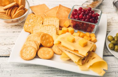 Beyaz ahşap arka planda gevrek kraker, kızılcık ve peynir tabağı.