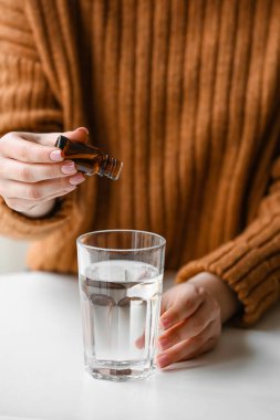 Kadın masadaki bardakta suya gerekli yağı ekliyor.