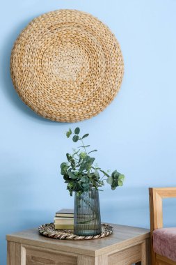 Okaliptüs dallı vazo ve mavi duvarın yanındaki masada kitaplar.