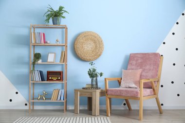 Masada okaliptüs dalları olan vazo, renk duvarına yakın koltuk ve kitaplık.