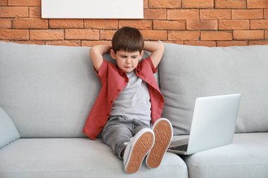 Evdeki kanepede dizüstü bilgisayarıyla çizgi film izleyen küçük çocuk.