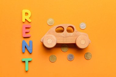 Bozuk paraları olan ahşap bir araba ve turuncu arka planda kelime RENT.