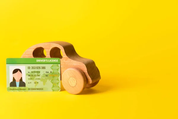Driving license and wooden car on yellow background