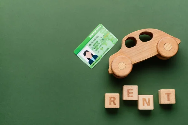 Wooden car with word RENT and driving license on green background