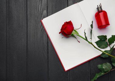Güzel kırmızı gül, parfüm ve karanlık ahşap zemin üzerine boş kitap.
