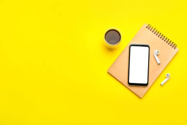 Bir fincan kahve, kulaklık, cep telefonu ve renkli arkaplan üzerine not defteri.
