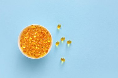 Renk arkaplanında A vitamini kapsülleri olan kase