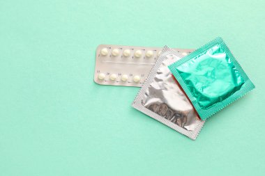 Renkli arka planda paketlenmiş prezervatifler ve doğum kontrol hapları
