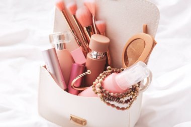 Hafif kumaş arka planında kozmetik ve aksesuarlı şık çanta, yakın plan