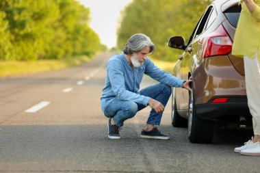 Dışarıdaki hasarlı arabanın yanında olgun bir adam var.