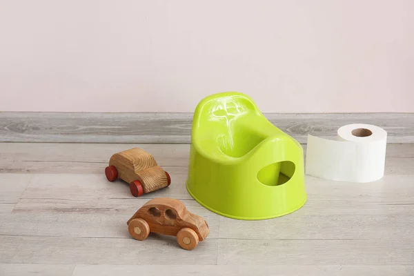 Potty, wooden cars and toilet paper roll on grey wooden floor near light wall