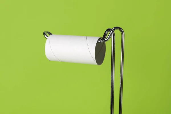 Holder with cardboard tube for toilet paper on green background, closeup