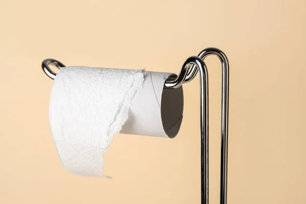 Modern holder with cardboard tube for toilet paper on beige background, closeup