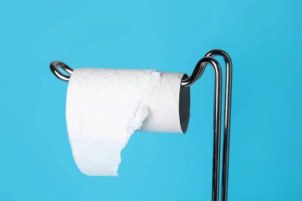 Modern holder with cardboard tube for toilet paper on blue background, closeup