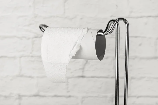 Holder with toilet paper cardboard tube on white brick background, closeup
