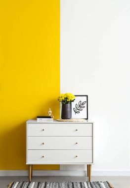Renk duvarının yanındaki çekmecelerin üzerinde kasımpatı olan koyu renkli vazo.
