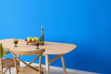 Mum, bardak ve elmalar renkli duvarın yanındaki modern masada.