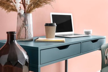 Renkli duvarın yanında dizüstü bilgisayarı ve vazosu olan gri masa.