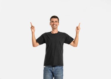 Şık tişörtlü yakışıklı genç adam arka plandaki bir şeyi işaret ediyor.