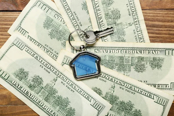 木の背景に家の形のキーチェーンとお金とキー — ストック写真