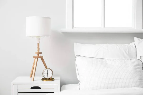 スタイリッシュなランプと目覚まし時計は 明るい寝室のインテリアのベッドサイドテーブルの上に — ストック写真
