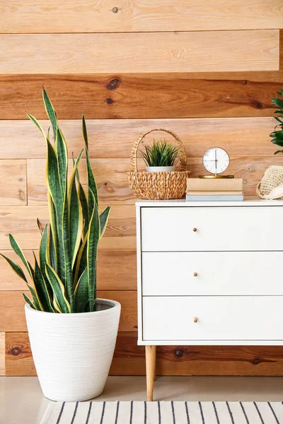 Odanın ahşap duvarının yanında şık bir çalar saat ve dekor olan çekmeceler.