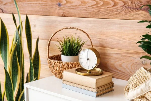 Ahşap duvarın yanındaki çekmecelerde kitaplar olan altın alarm saati.