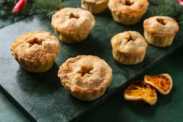 Board with tasty mince pies on green background