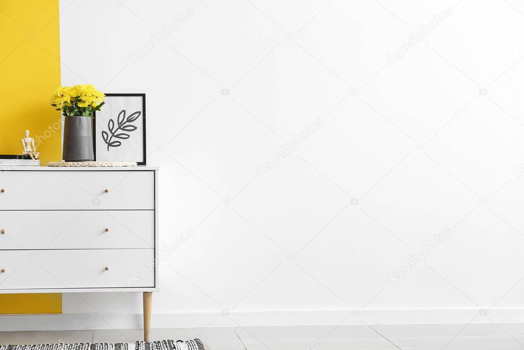 Vase with yellow chrysanthemums on chest of drawers near color wall
