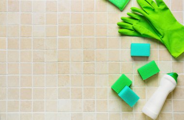 Yeşil temizlik süngerleri, eldivenler ve fayans üzerinde bir şişe deterjan.