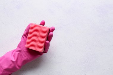 Kadın eli eldivende, arka planda pembe temizlik süngeri var.