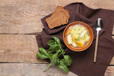 Bir kase lezzetli hamur çorbası, ahşap arka planda ekmek ve fesleğen.