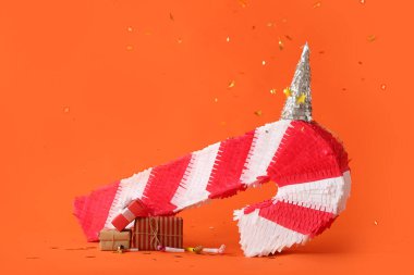 Parti şapkalı baston şeklinde Meksika pinyatası ve renkli arka planda hediyeler.