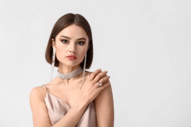 Beyaz arka planda şık mücevherleri olan genç bir kadının portresi.