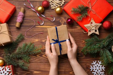Hediye kutularıyla kadın elleri, köknar dalları ve ahşap arka planda süslemeler, yakın plan.