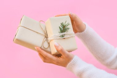 Pembe arka planda hediye kutuları olan kadın eller, yakın plan.