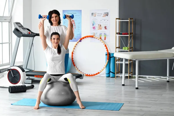 Junge Frau Mit Kurzhanteln Auf Fitball Und Physiotherapeutin Reha Zentrum — Stockfoto