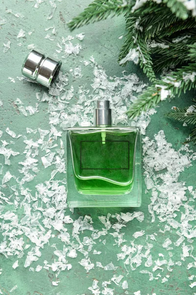 Bir şişe parfüm, köknar dalları ve arka planda kar.