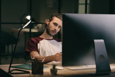 Genç adam akşam geç saatlerde ofiste bilgisayar kullanıyor.
