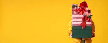 Noel Baba şapkalı adam sarı arka planda bir sürü Noel hediyesi tutuyor ve mesaj için yeri var.