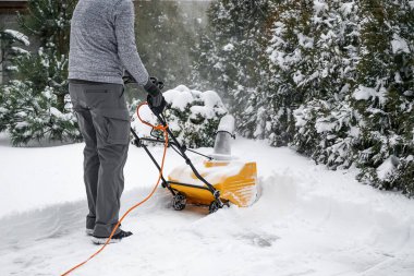 Man with machine removing snow in yard clipart