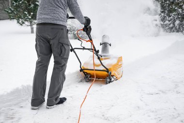 Man with machine removing snow in yard clipart